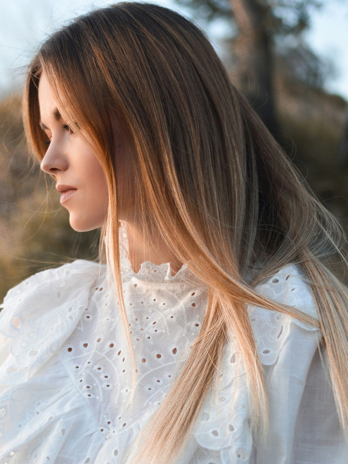 Side view of a woman outside in natural surroundings showing her straight balayage with brunette hair melting into blonde shades