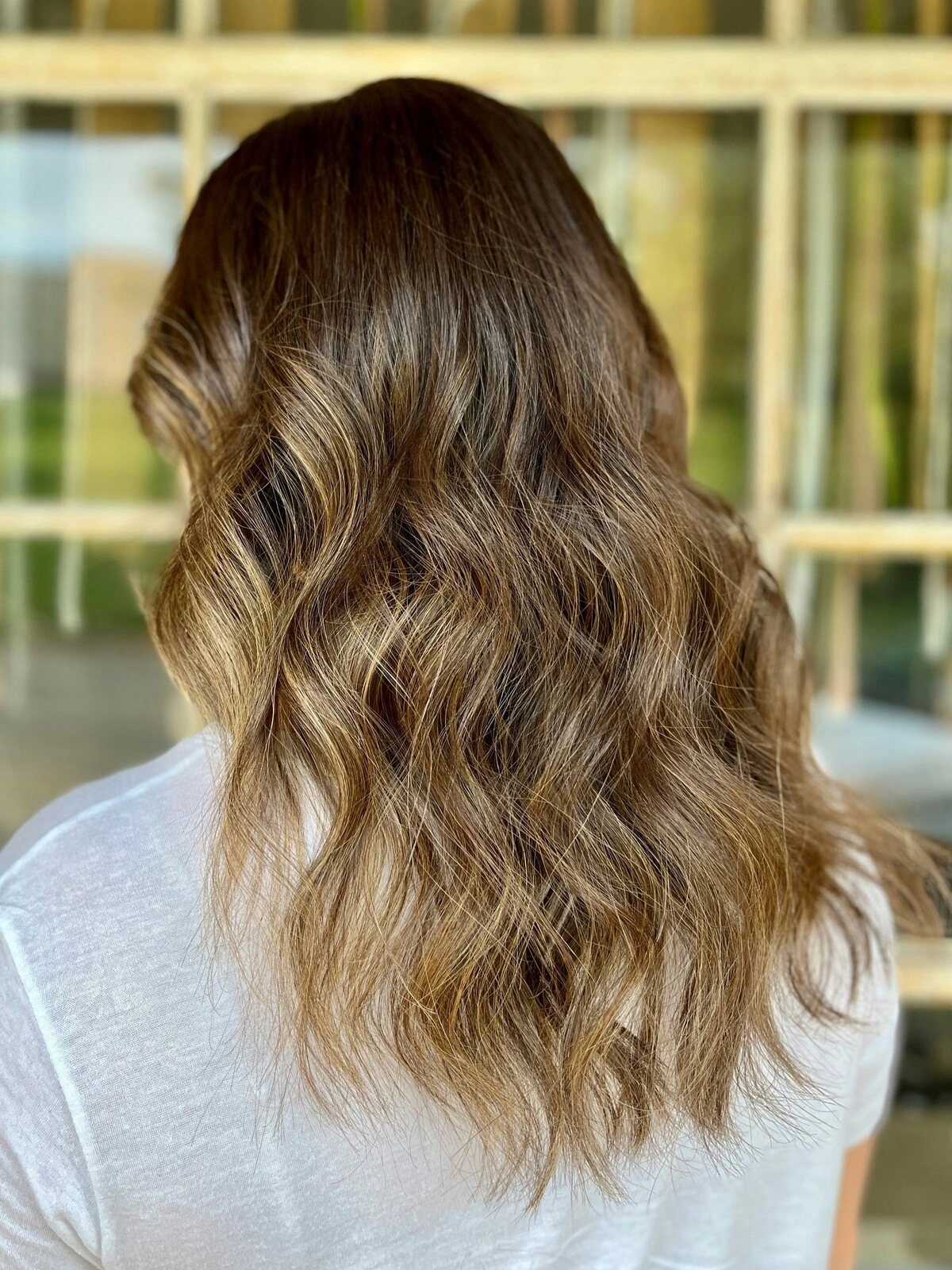 Back view of a woman’s head showing a wavy balayage with dark hair blending into warm tones