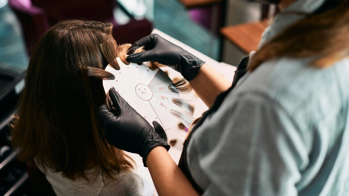Close-up of a colourist holding hair swatches against a client’s head to select shades for a balayage treatment