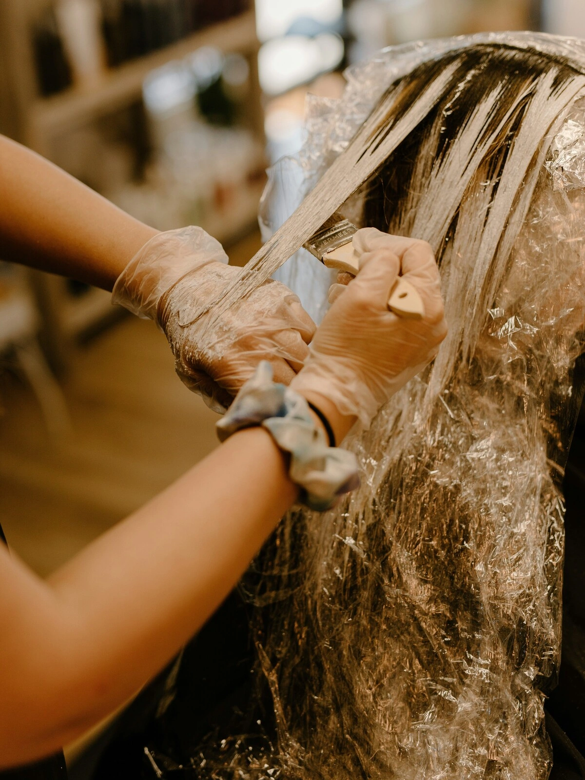 A colourist wearing gloves applies dye to a client’s hair using a brush as part of a balayage treatment