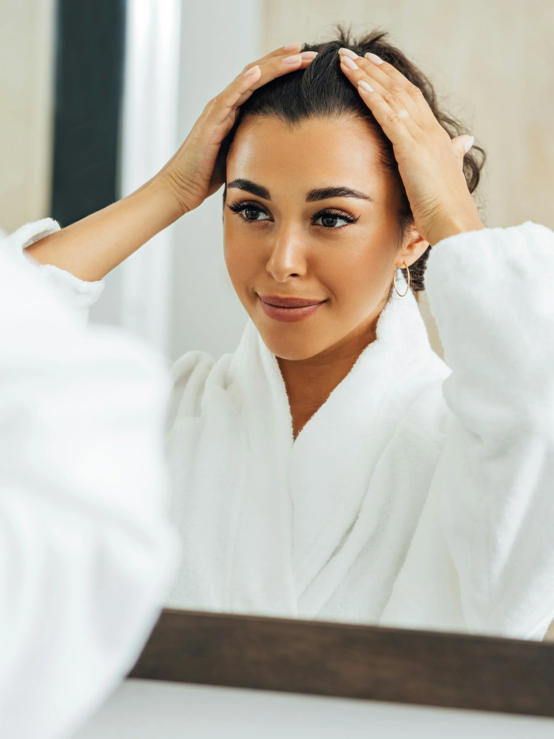 Woman holding her hair back off her face and smiling as she looks in the mirror