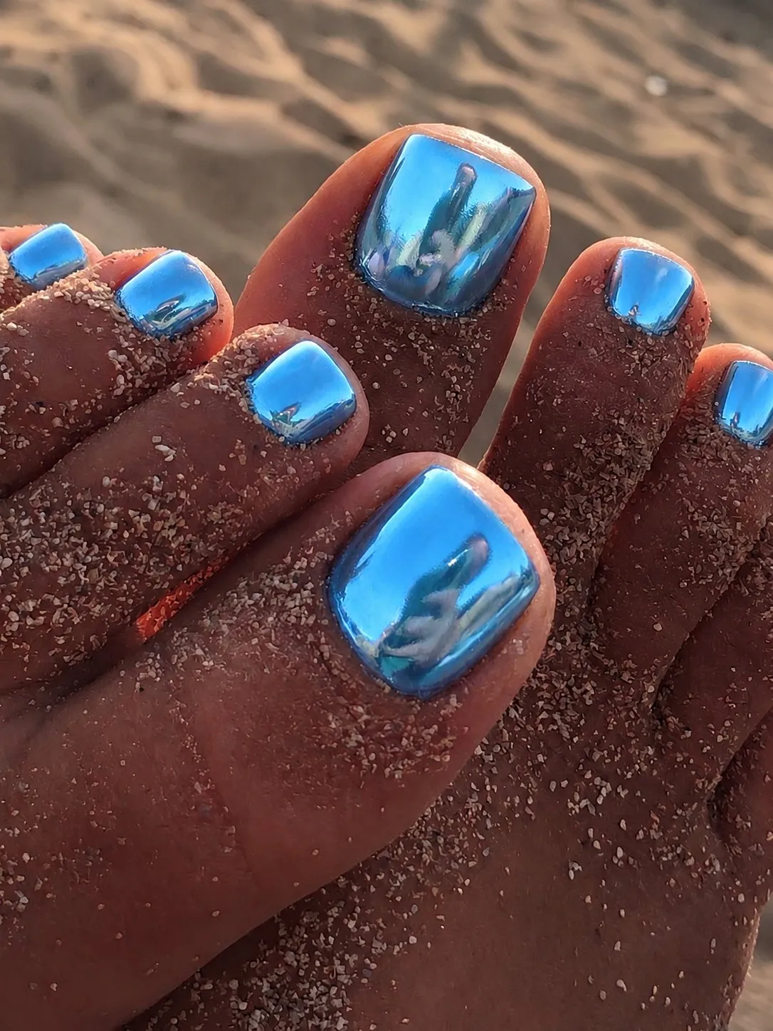 Metallic ocean blue chrome pedicure on sandy feet at the beach