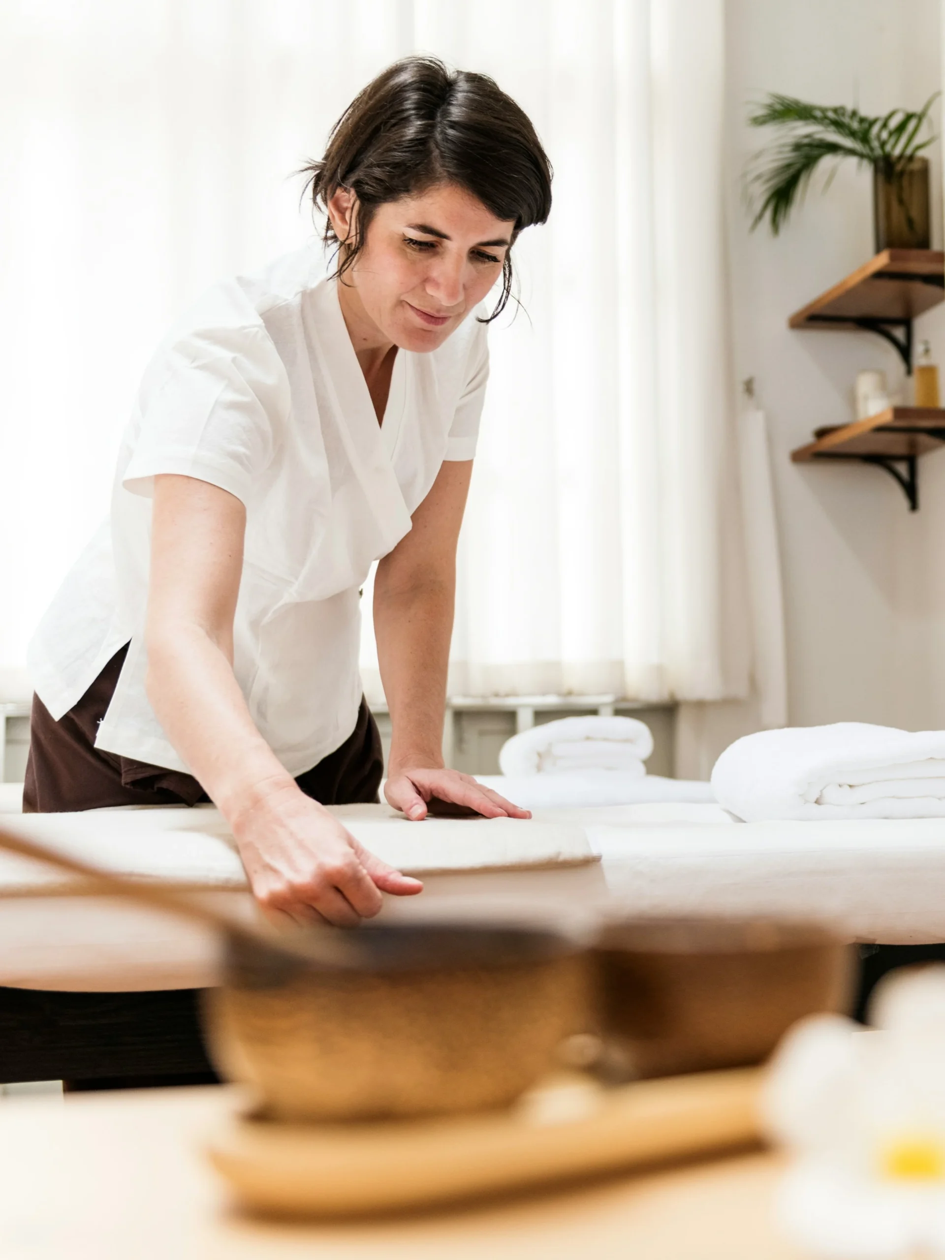 A reflexologist prepares a room for treatment, smoothing the bed with flowers and a candle in the foreground