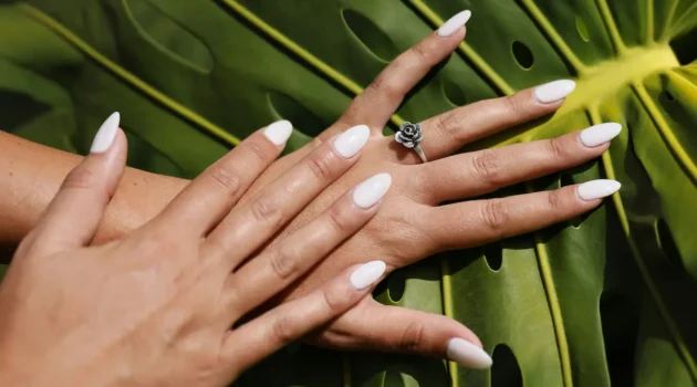 Studio shot of fresh almond-shaped nude-colour acrylic nails on a palm leaf backdrop