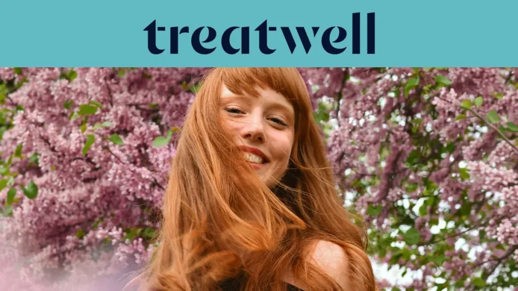 A woman with long copper-red hair and a fringe smiling in the sunshine, with pink blossom trees in the background. The Treatwell logo sits on a teal banner above.