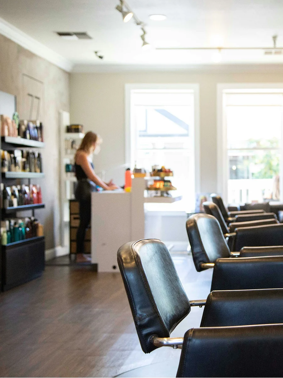 Interior shot of a clean, bright and well-ventilated hair salon showing big windows, black chairs and shelves of products