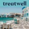 The Little Venice waterfront in Mykonos Town: whitewashed houses with colourful wooden balconies at the sea's edge, the turquoise Aegean beyond, and white and teal café tables set out across a stone-paved terrace in the foreground.