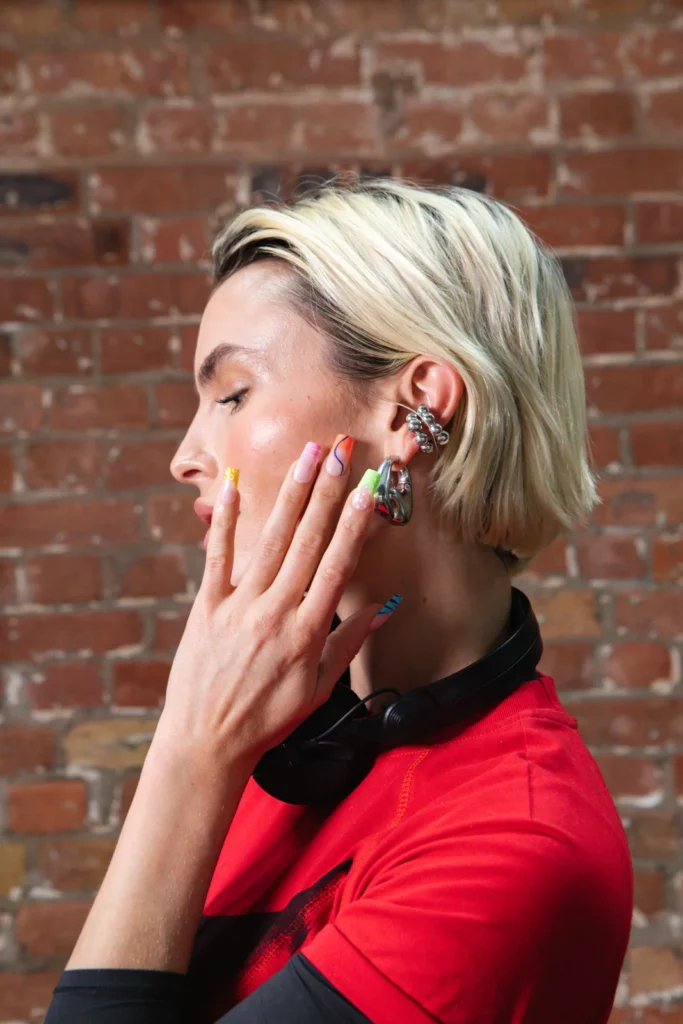 DJ and actress Rex Adams in profile, headphones round the neck, showing the colourful electric mani’s neon French tips