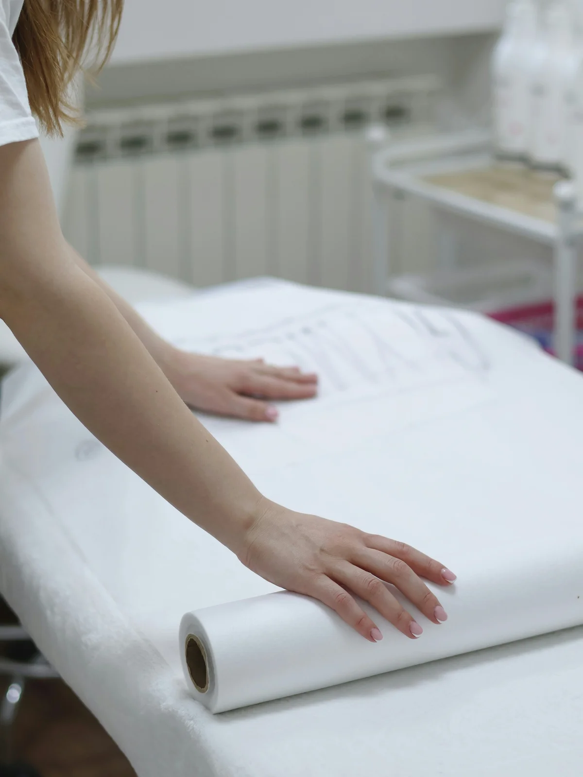 Close up of a therapist's arms as she unrolls a clean sheet of paper onto a salon bed in preparation for a treatment