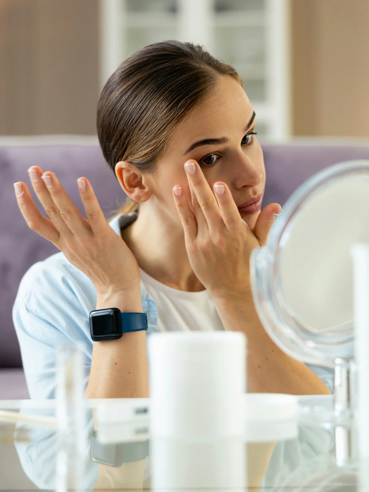 A woman sits at a table delicately applying moisturiser and oils to her face and brows