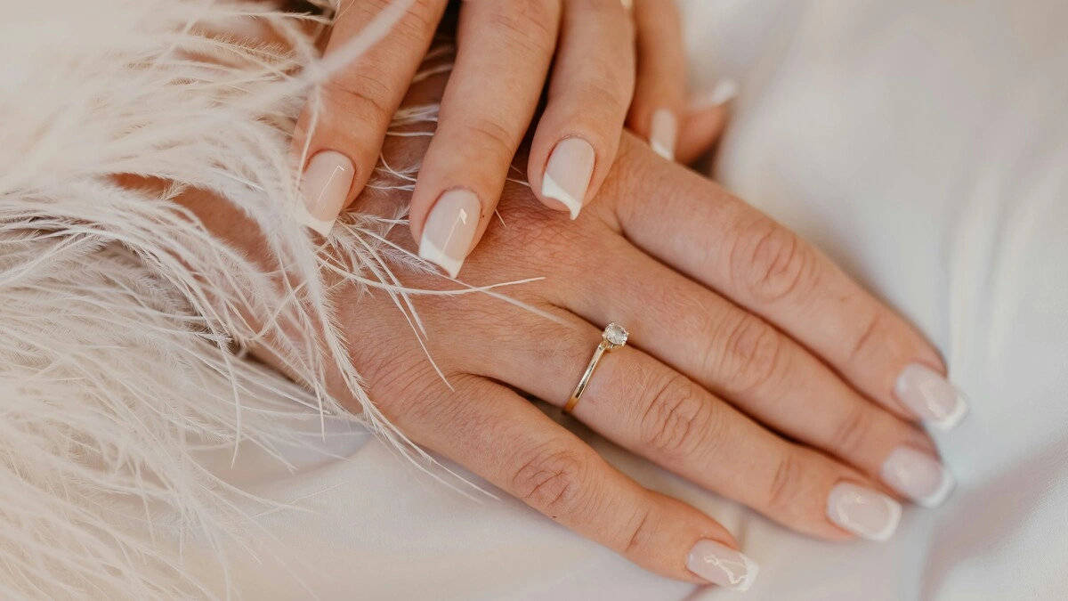 Classic white French tip manicure on natural square-shaped nails resting on white fabric