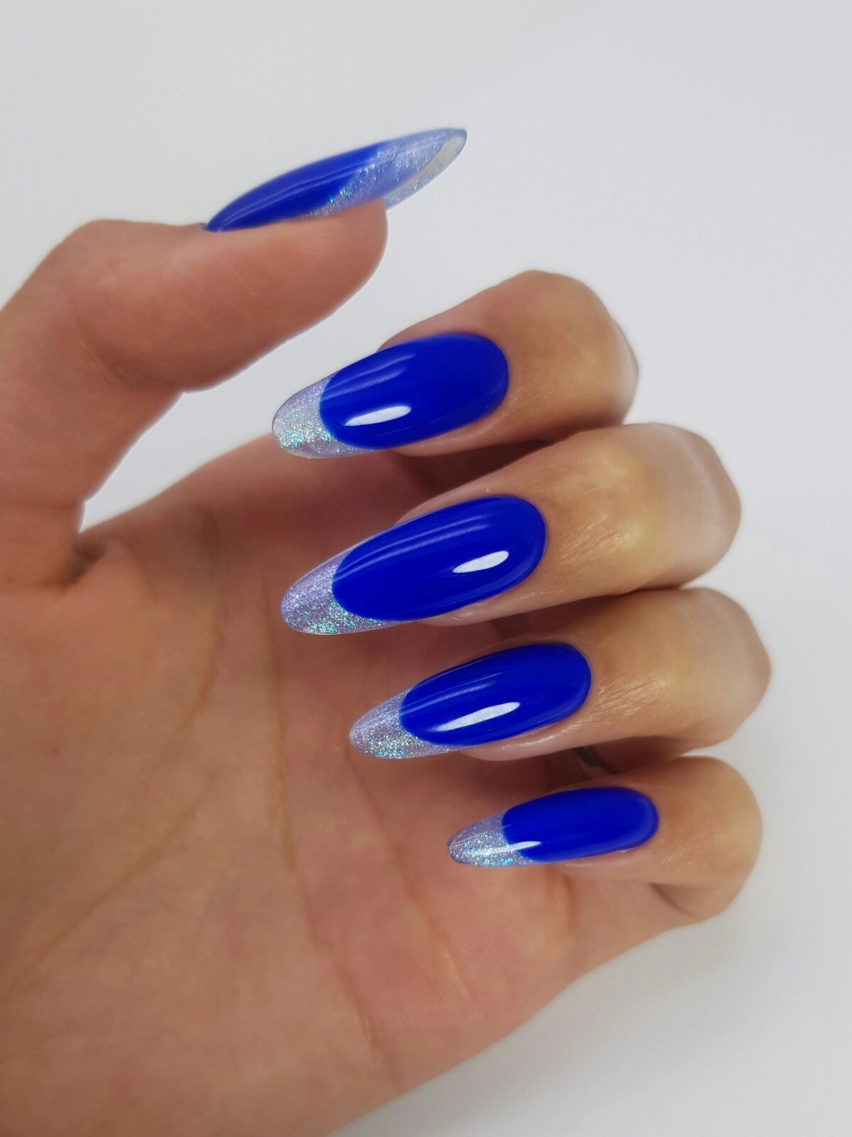 A woman’s hand showing a bold French tips manicure with a bright blue base and silver metallic tips on long almond nails