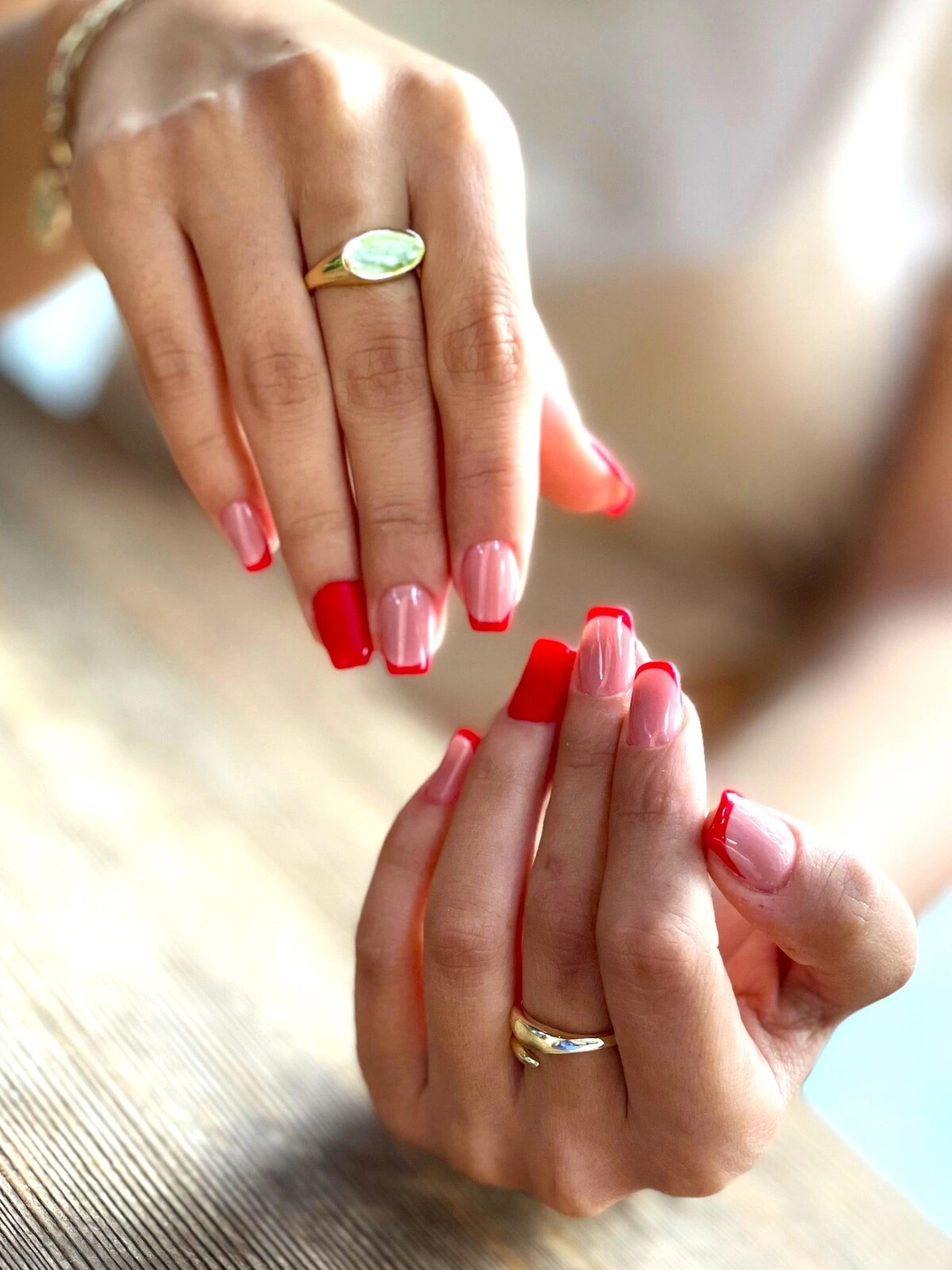 A French tips manicure on squoval nails with a baby pink base and red tips with fully red ring finger nails