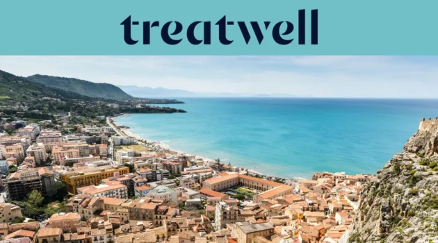 A sweeping view over a Sicilian coastal town, with terracotta-roofed old buildings, a crescent of sandy beach, clear turquoise sea and a rocky headland rising to one side.