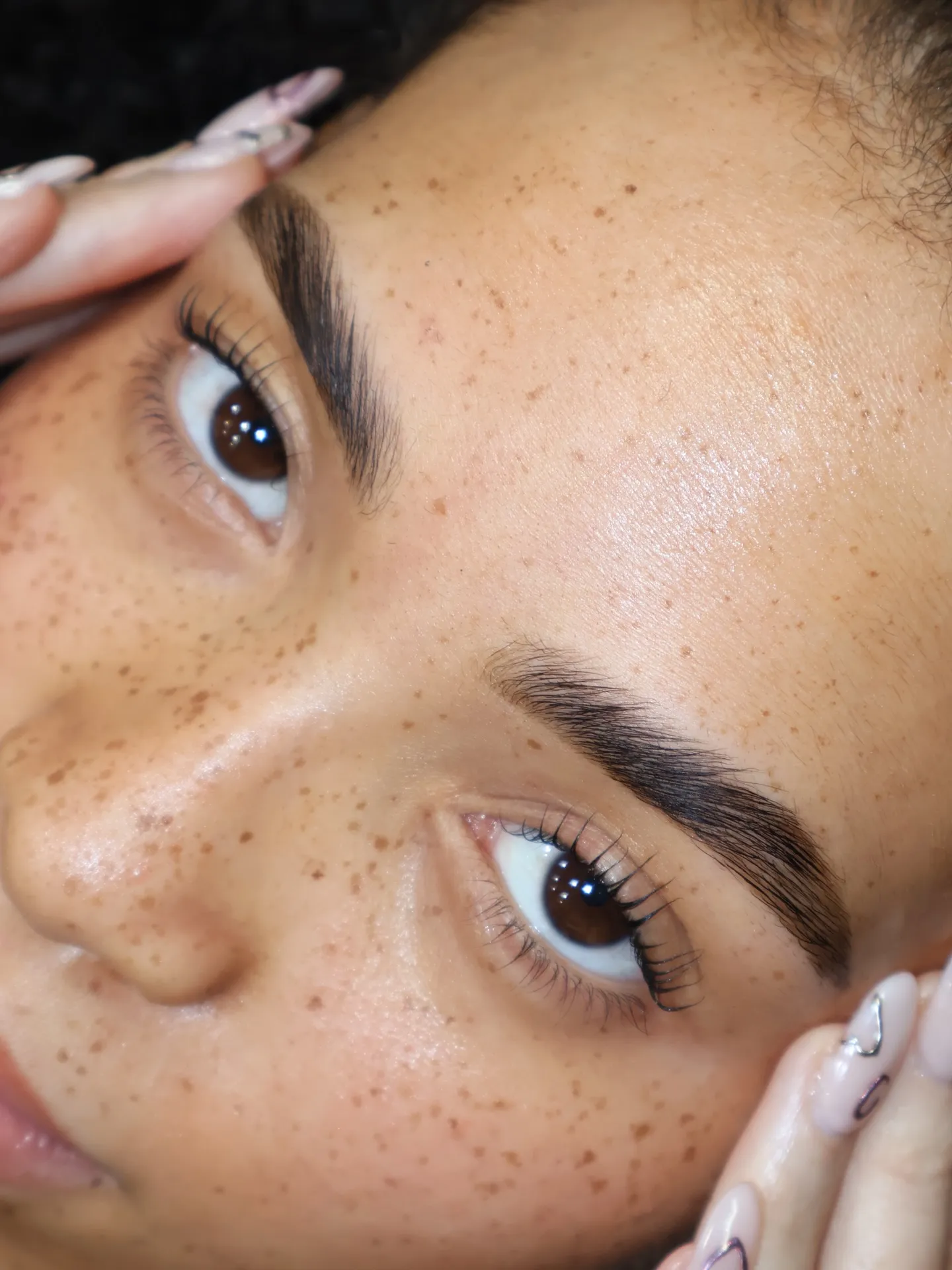 Close-up of naturally lifted lashes after a Korean lash lift, soft separated curl with airy texture on freckled skin