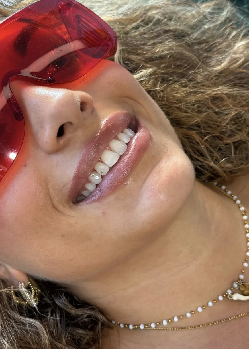 Close-up of a smile showing two small crystal tooth gems on lower teeth, summer portrait