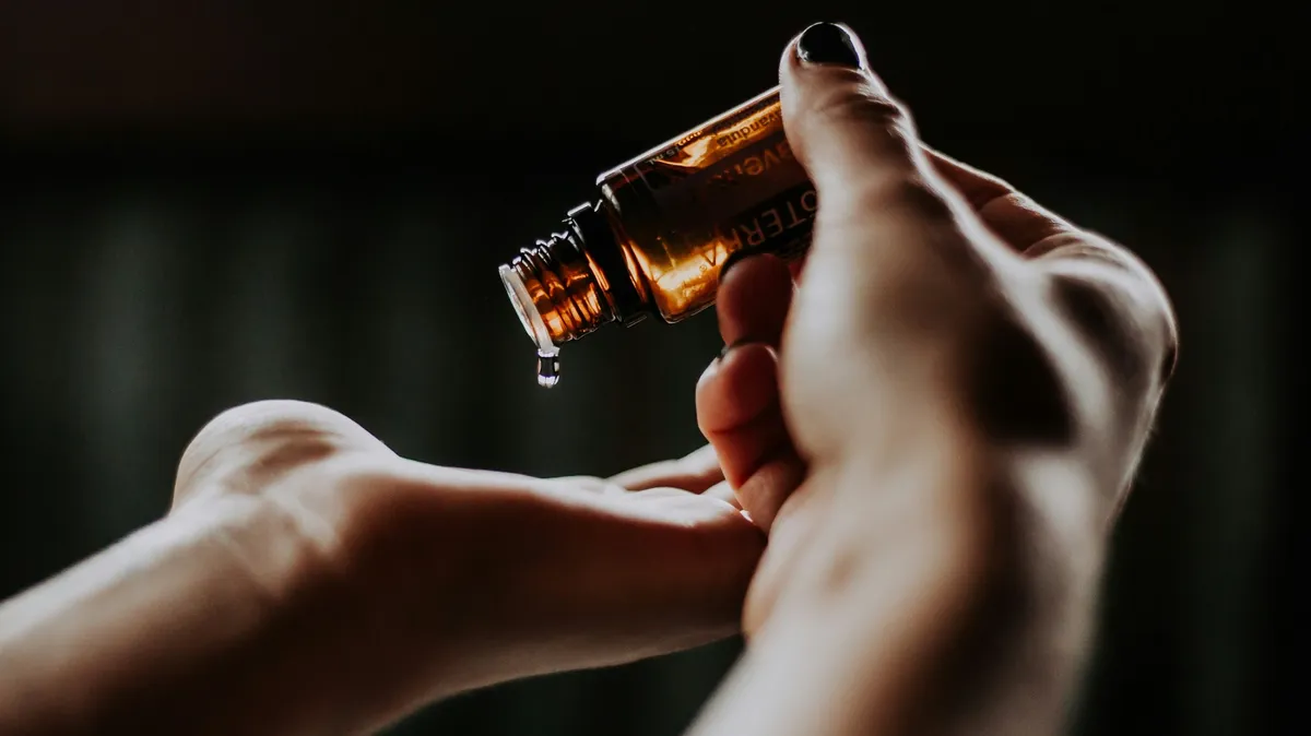 Close-up of a therapist's hands as one hand pours drops of oil from a glass bottle into the palm of the other hand